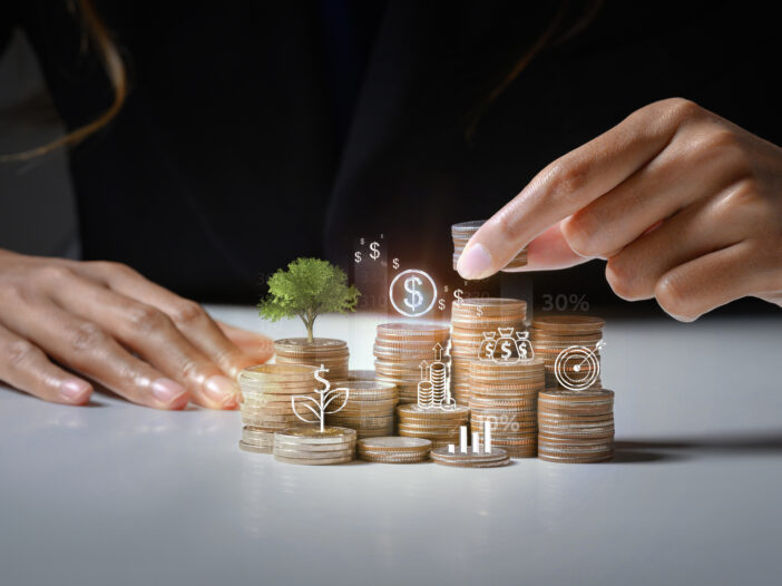 Businessman putting coin on stack with growing small tree symbolizing investment growth and saving money